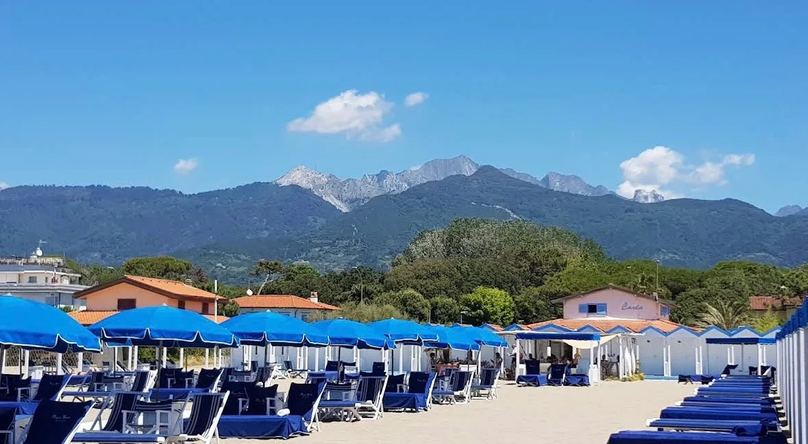 Lo stabilimento Bagno Carla visto dalla spiaggia con cabine bianche, ombrelloni blu e Alpi Apuane sullo sfondo, Vittoria Apuana